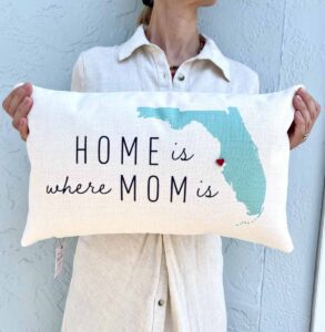 Person holding a pillow that says "home is where the mom is"